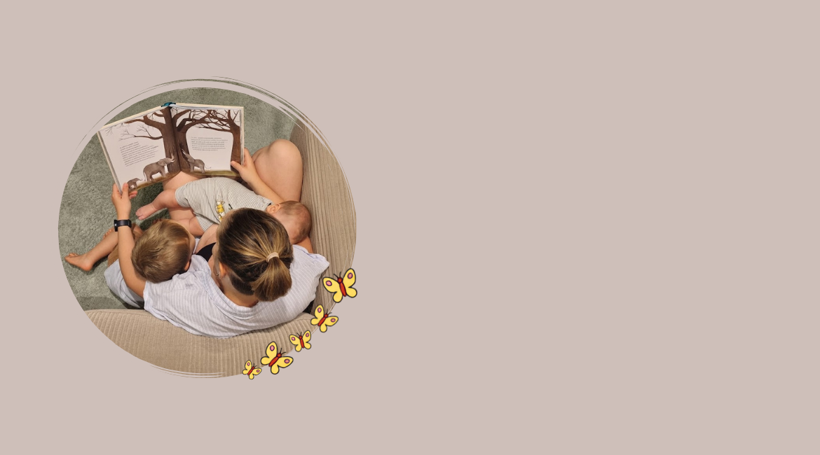 Nell'immagine si vede una mamma con due bambini, di cui uno al seno, che sta leggendo un libro. La foto è ripresa dall'alto e lo sfondo è color tortora.