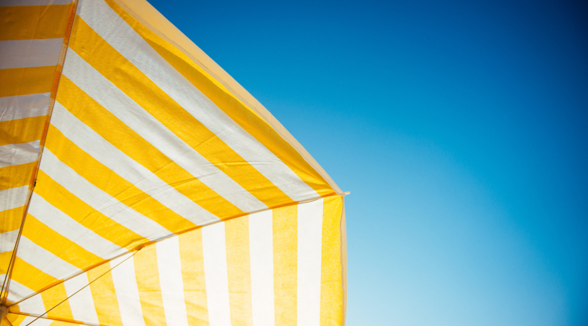 Nell'immagine si vede un ombrellone a righe gialle e bianche che si staglia sul cielo azzurro.