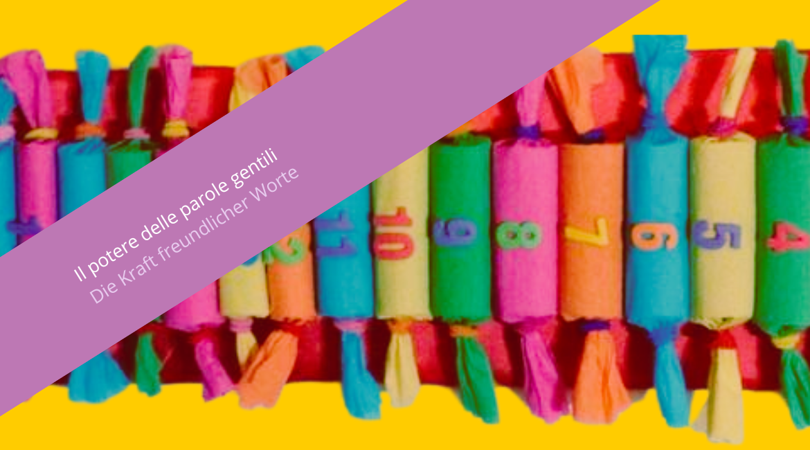Nell'immagine si vede un calendario fatto con pacchettini cilindrici colorati e numerati. Lo sfondo è giallo. Sovrapposta all'immagine si vede una fascia viola con la scritta "Il potere delle parole gentili. Die Kraft freundlicher Worte".