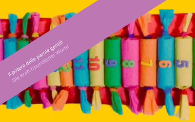 Nell'immagine si vede un calendario fatto con pacchettini cilindrici colorati e numerati. Lo sfondo è giallo. Sovrapposta all'immagine si vede una fascia viola con la scritta "Il potere delle parole gentili. Die Kraft freundlicher Worte".