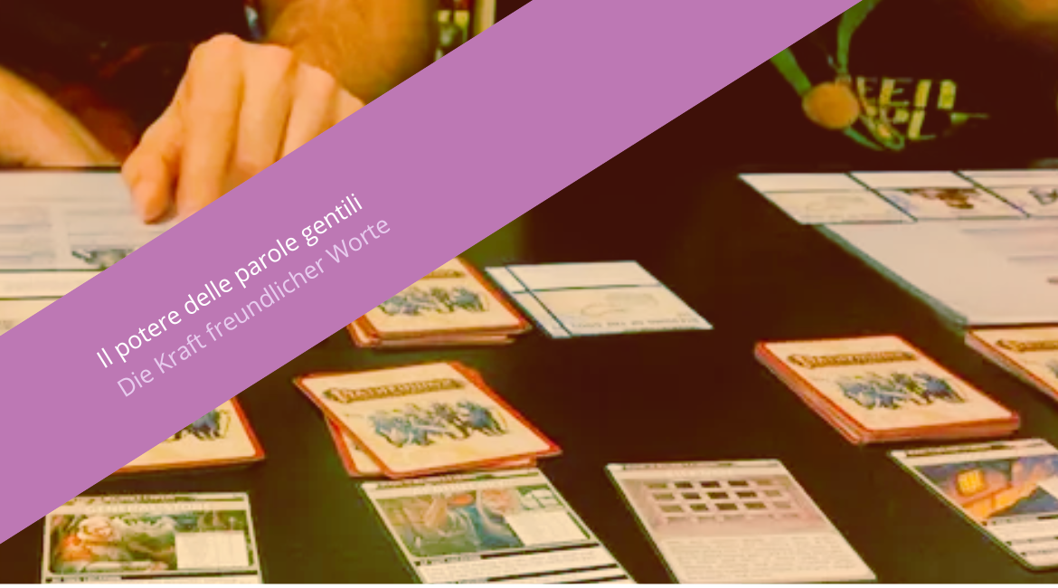 Nell'immagine si vede un tavolo con delle carte da gioco e una mano che le svela. Sovrapposta all'immagine si vede una fascia viola con la scritta "Il potere delle parole gentili. Die Kraft freundlicher Worte".