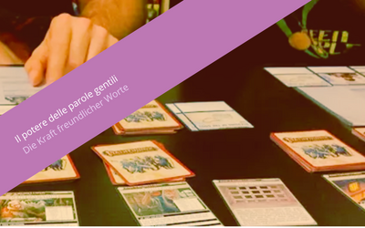 Nell'immagine si vede un tavolo con delle carte da gioco e una mano che le svela. Sovrapposta all'immagine si vede una fascia viola con la scritta "Il potere delle parole gentili. Die Kraft freundlicher Worte".