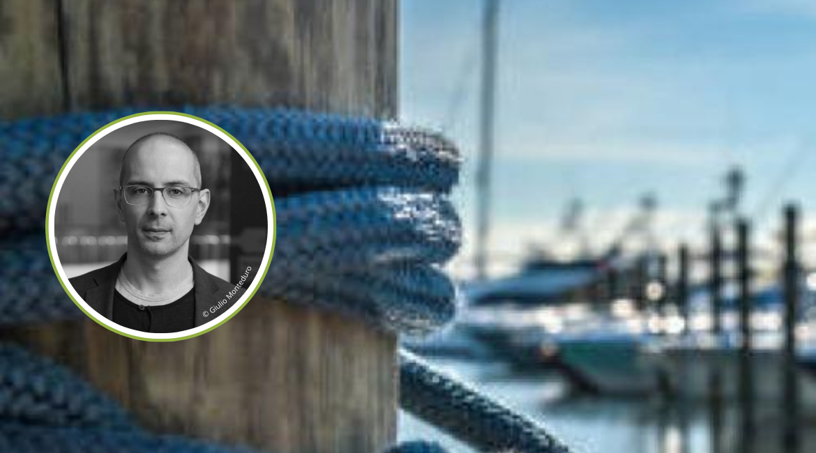 Sullo sfondo dell'immagine di un porto con barche ormeggiate, si trova la foto in bianco e nero di Stefano Zangrando.